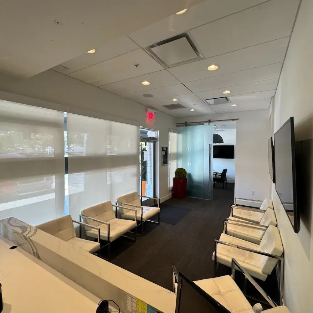 A small waiting room with white chairs and a reception desk in the foreground.