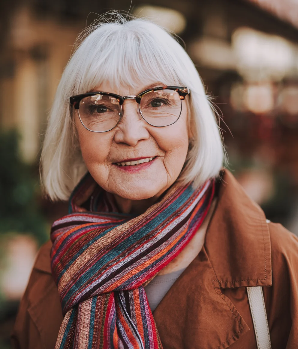 A woman smiling wearing glasses and a striped scarf.
