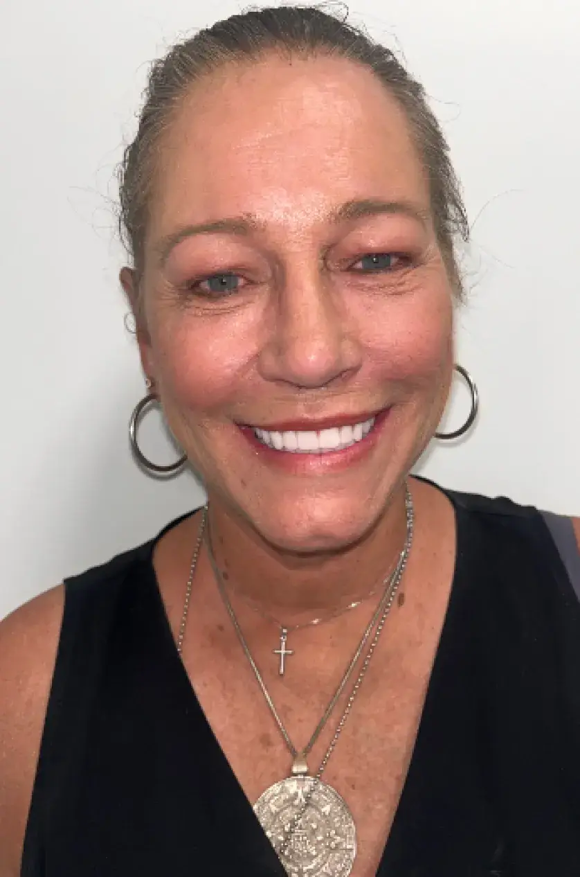 Smiling woman wearing hoop earrings and layered necklaces against a plain background.