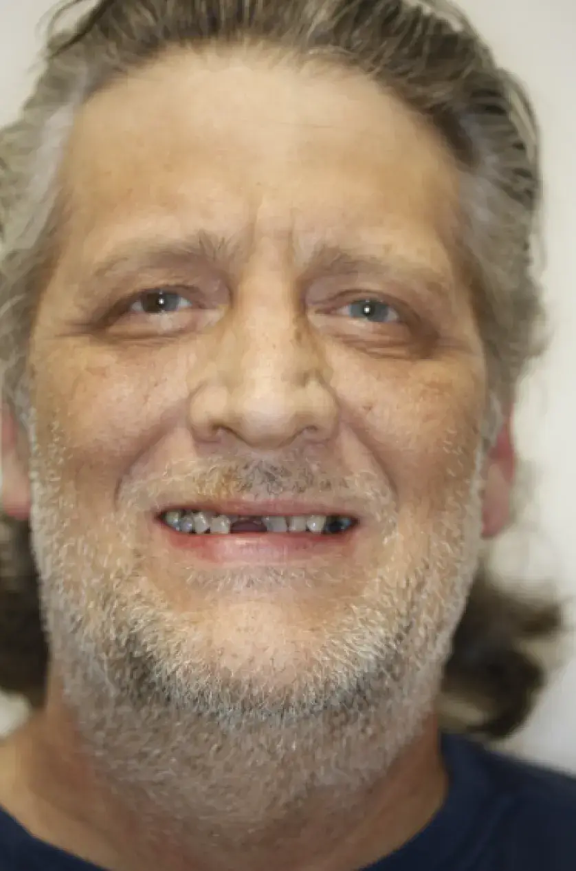 Smiling man with a beard and long hair, wearing a dark shirt, facing the camera.