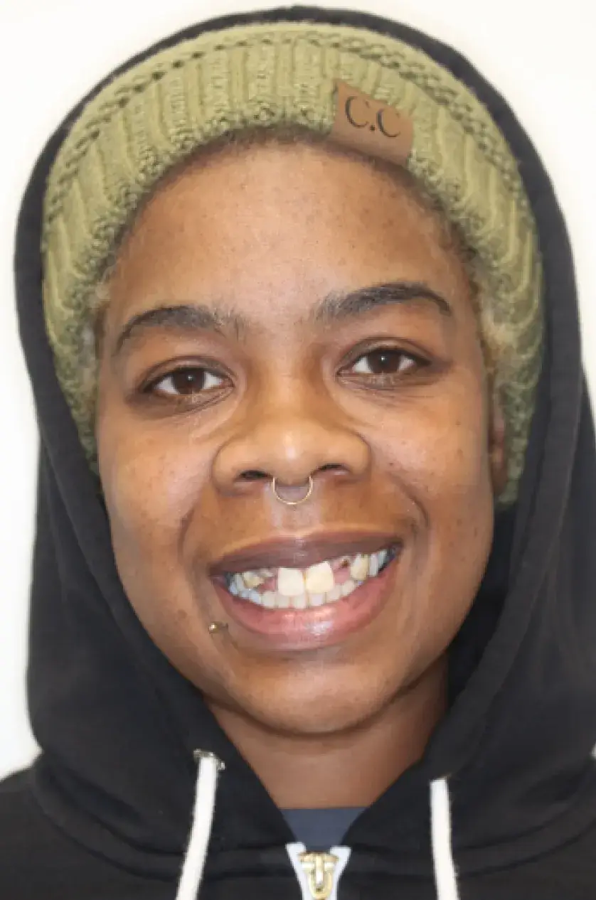 Person wearing a green knit hat and black hoodie, smiling at the camera.