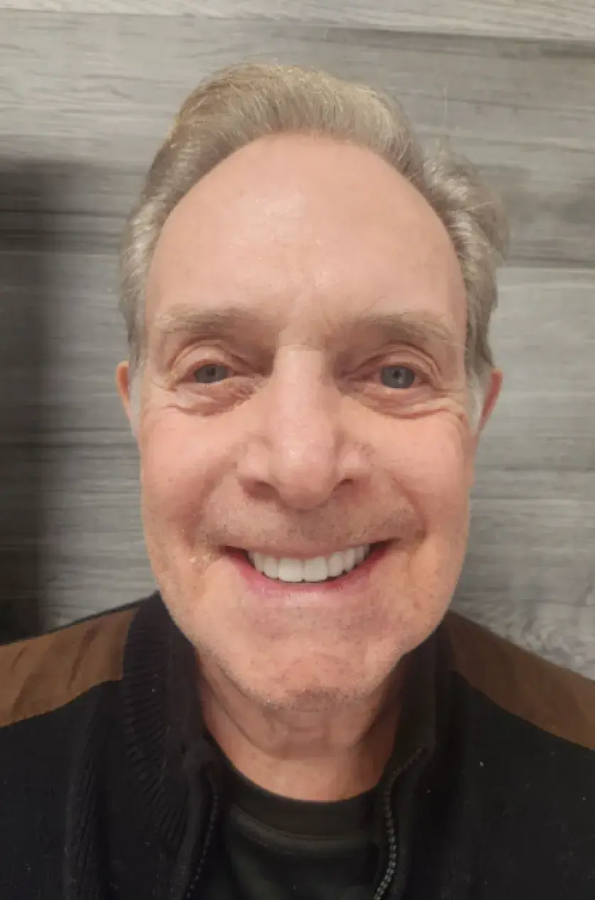 A person smiling directly at the camera, wearing a black sweater.