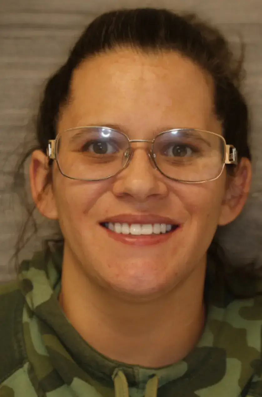 A person wearing glasses and a camo hoodie smiles at the camera.