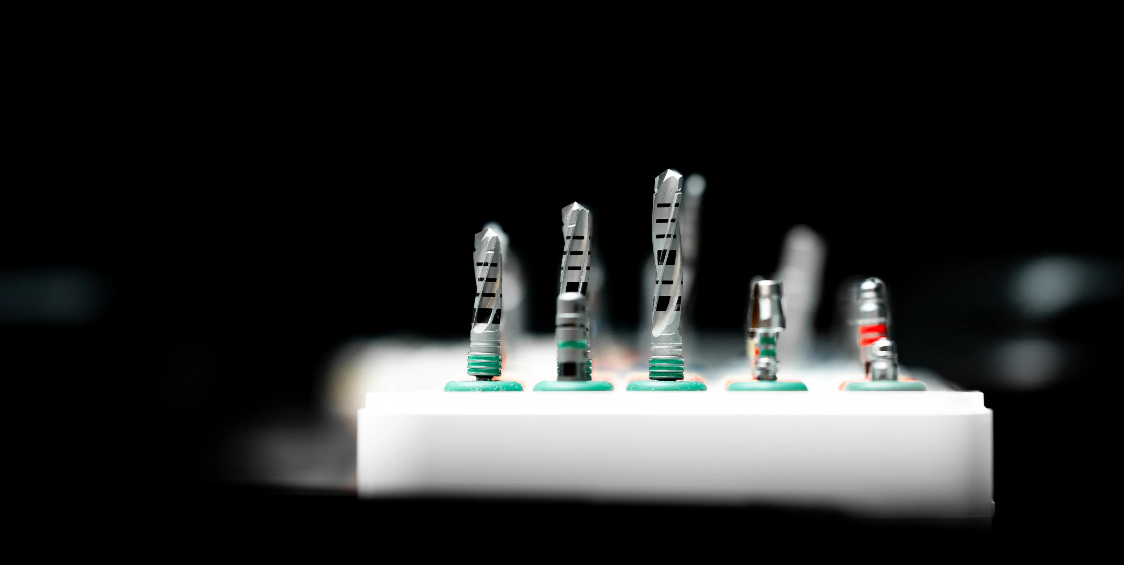 Close-up of dental drill bits of various sizes on a white holder against a black background.