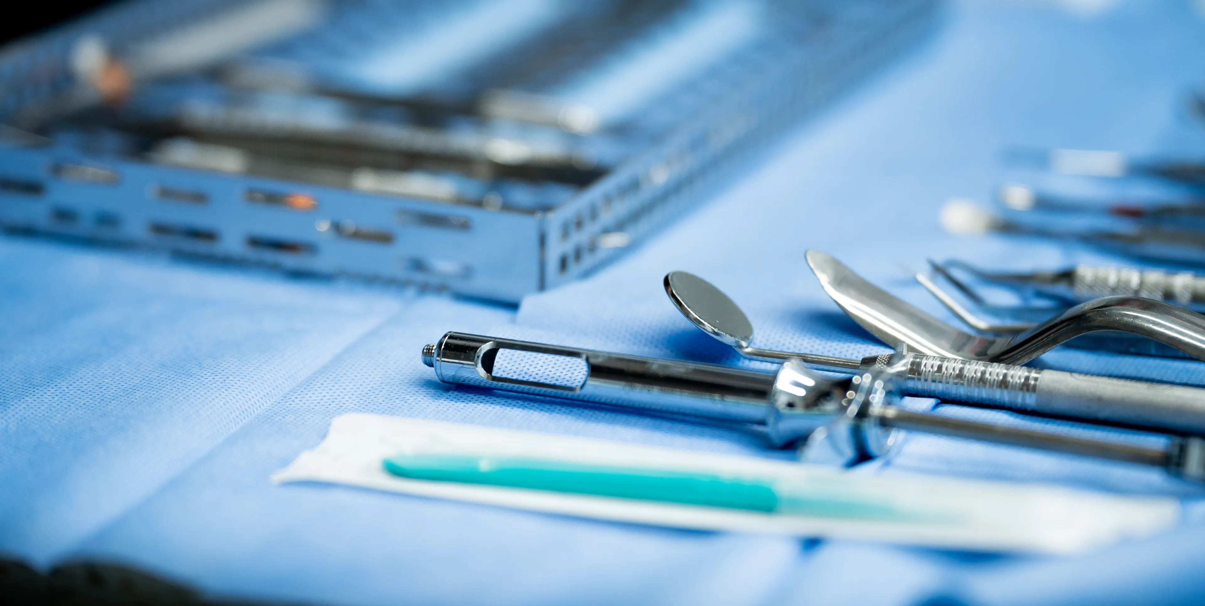 Dental tools arranged on a blue cloth, including a mirror, syringe, and other instruments.