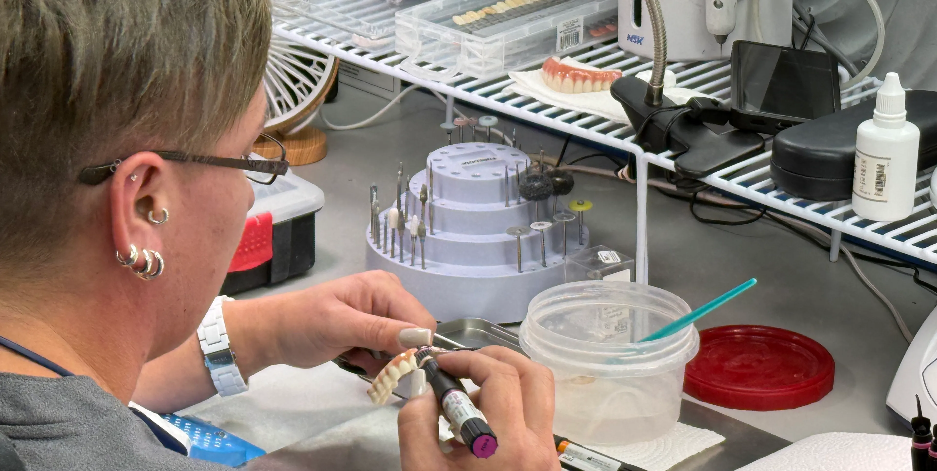 A person wearing glasses works on a dental mold at a laboratory table.