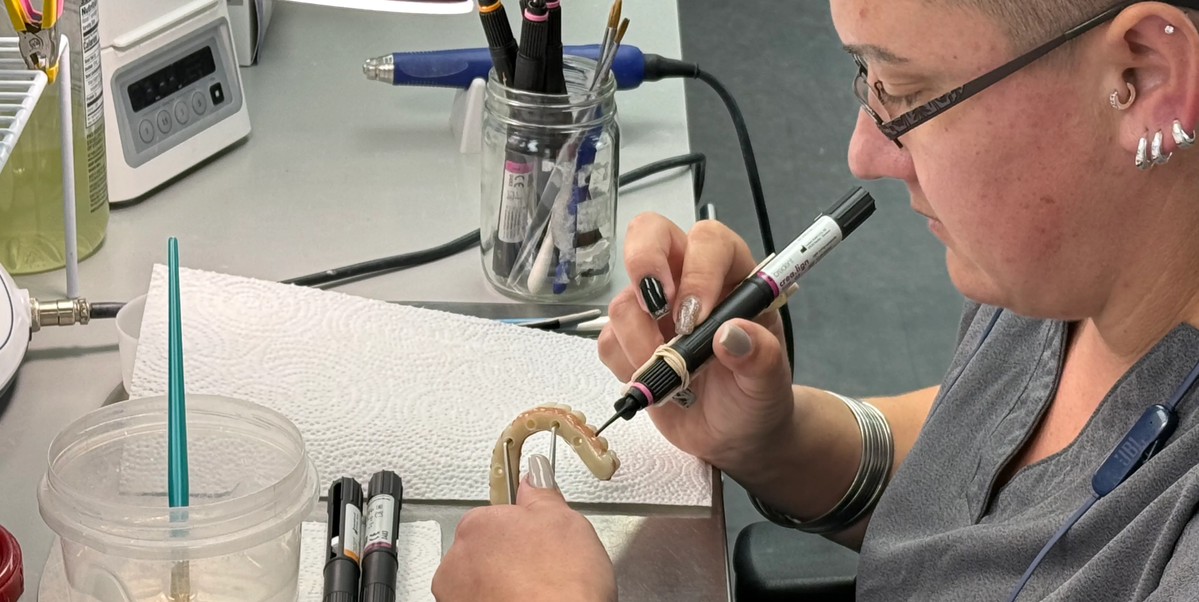 A person is painting a dental model with a color marker on a desk.