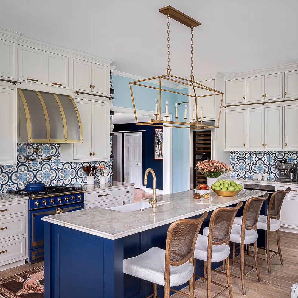 Modern kitchen with blue island, marble countertop, brass fixtures, patterned backsplash, and four wooden stools.