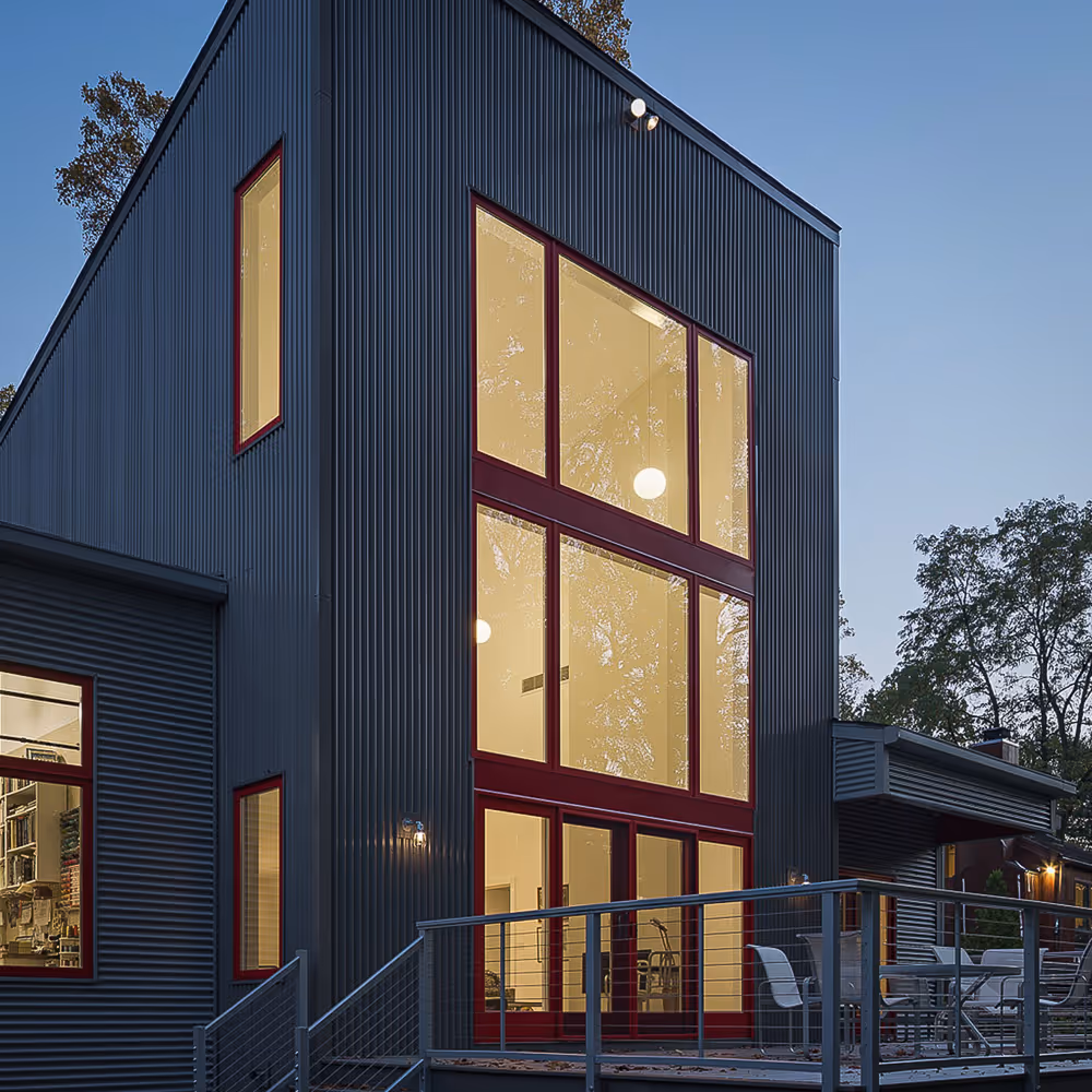 Modern two-story building with large illuminated windows and metal siding at dusk.