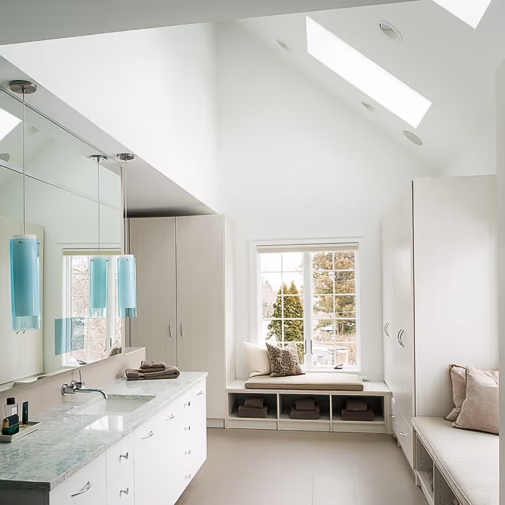 Bright modern bathroom with white cabinetry, marble countertop, blue pendant lights, and cushioned window seating.