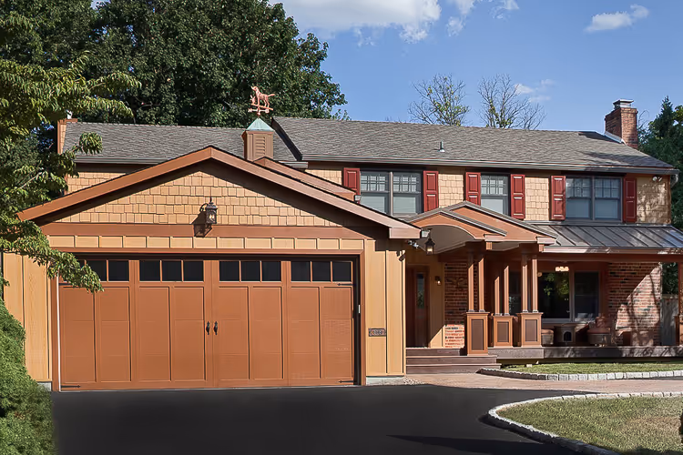 Two-story suburban house with tan siding, red shutters, a brown garage door, and a front porch with columns.