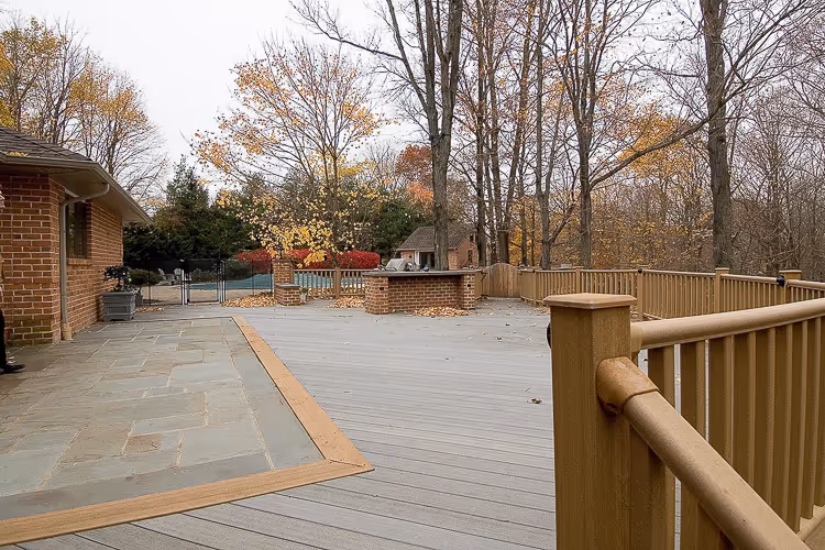 Large wooden deck with built-in brick grill and wooden railing, surrounded by trees with autumn foliage.