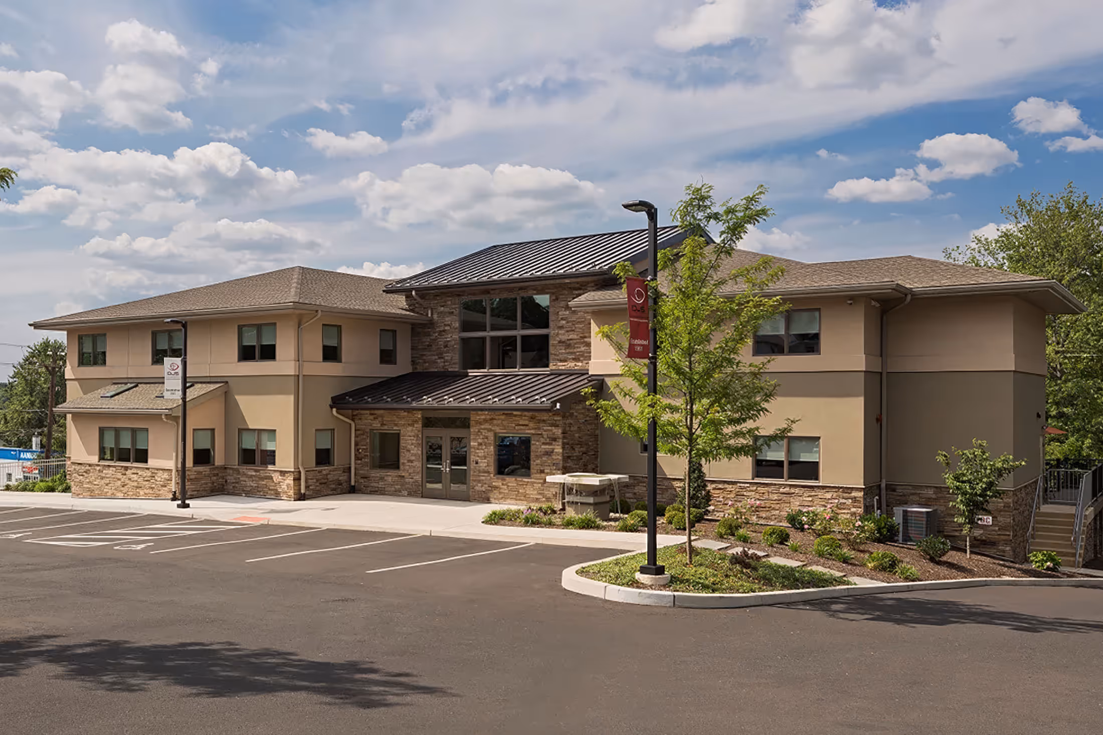 Two-story commercial building with beige walls, stone accents, and a metal roof under a partly cloudy sky.