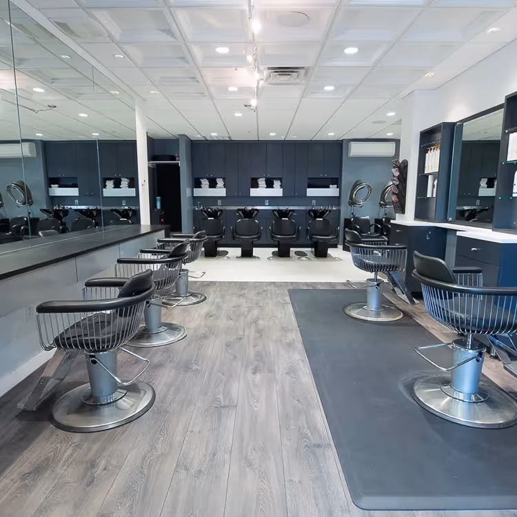 Modern hair salon with black styling chairs, large wall mirrors, and washing stations at the back.