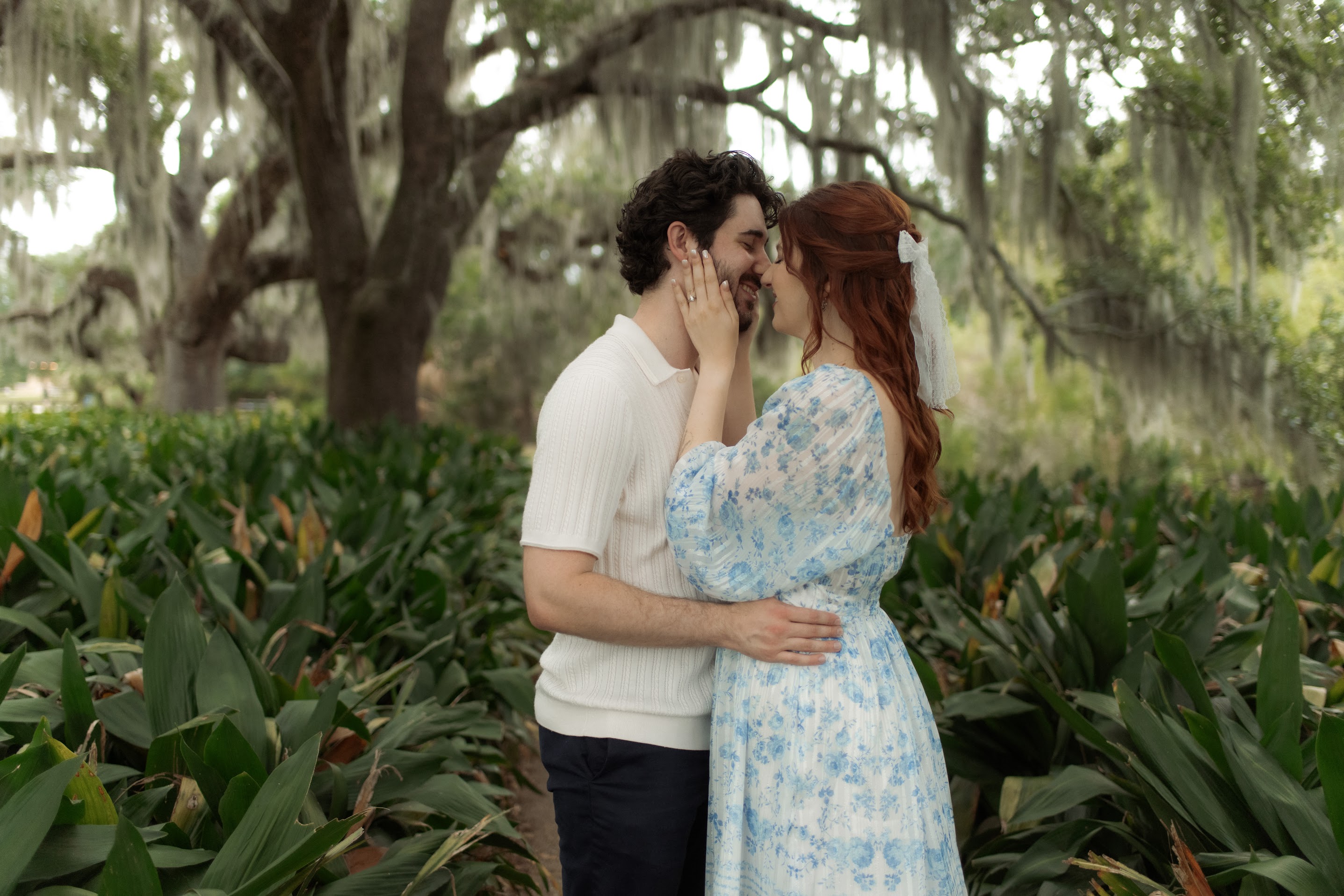 Couple embracing closely outdoors surrounded by greenery and large trees with hanging moss.