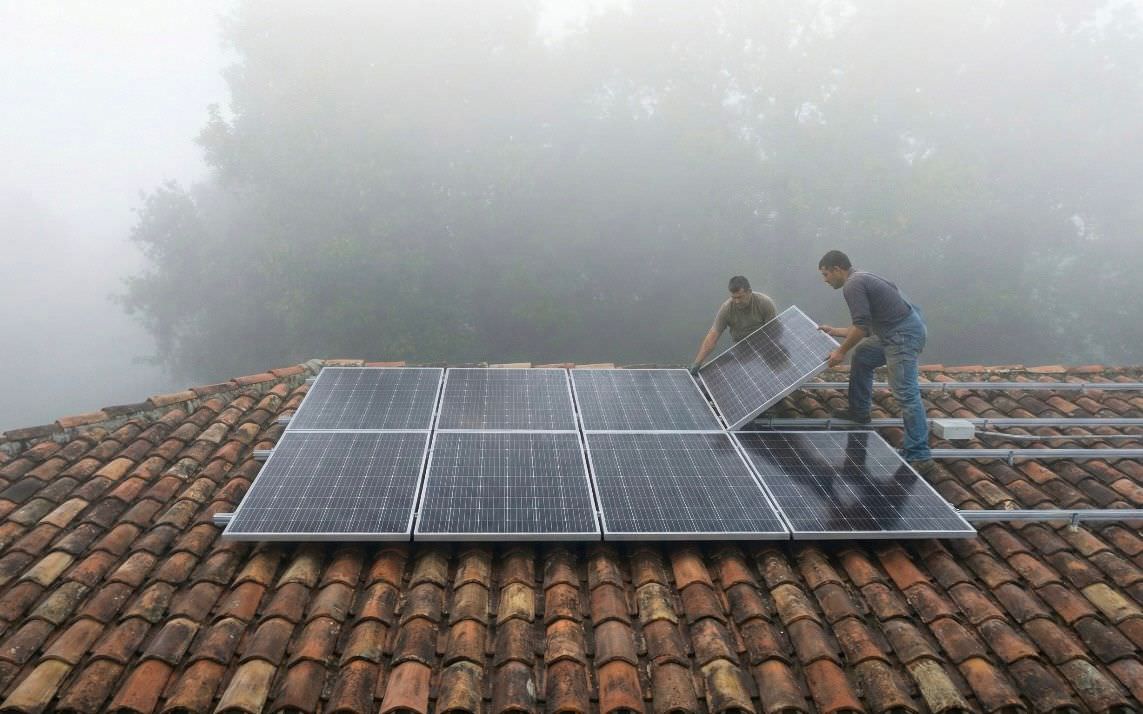 Two workers installing solar panels on a tiled rooftop in foggy weather.