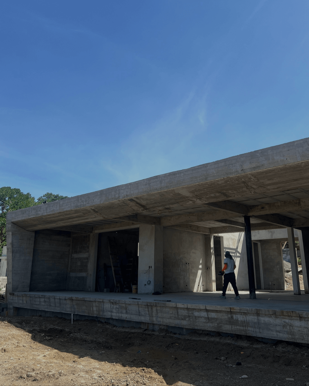 Person walking inside an unfinished concrete building under clear blue sky.