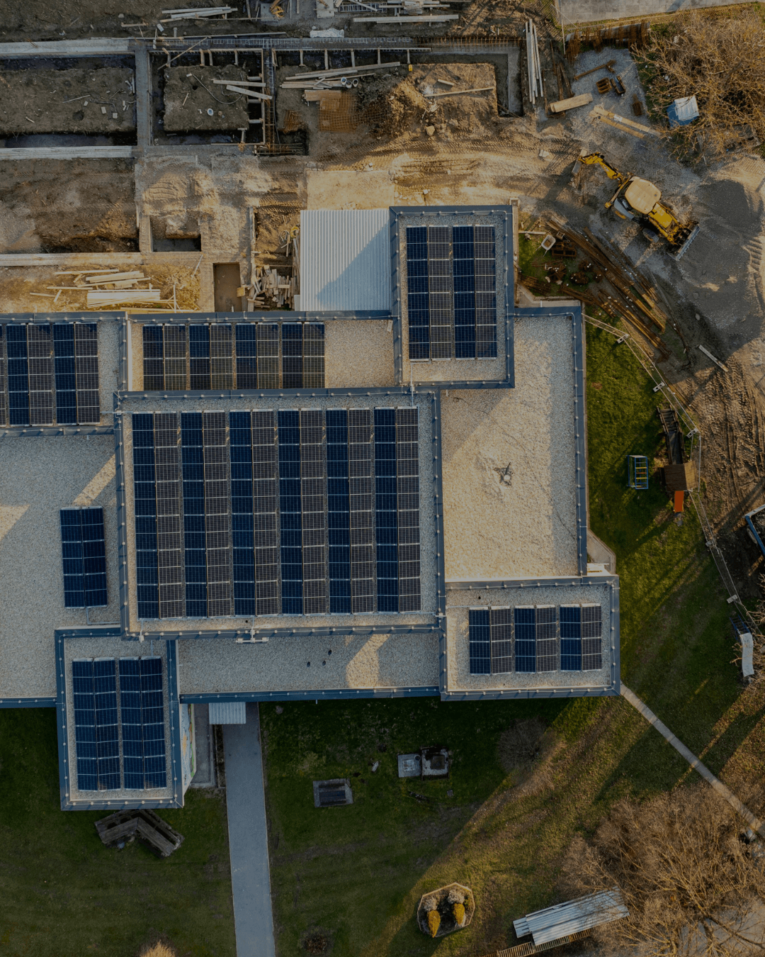Aerial view of a building with multiple solar panel arrays on its flat roof and surrounding construction and green grass areas.