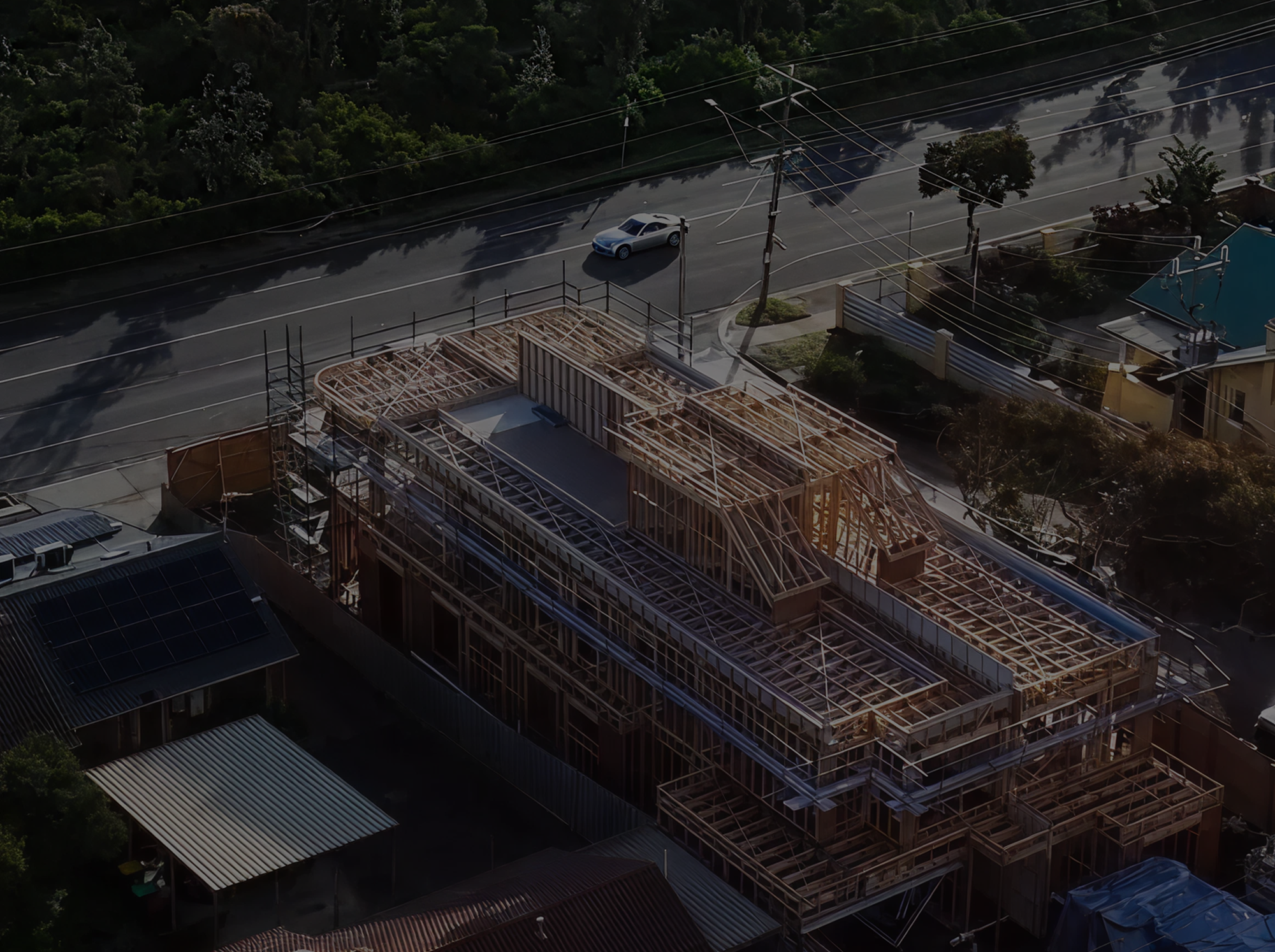 Aerial view of a large wooden building frame under construction next to a road with a car passing by.