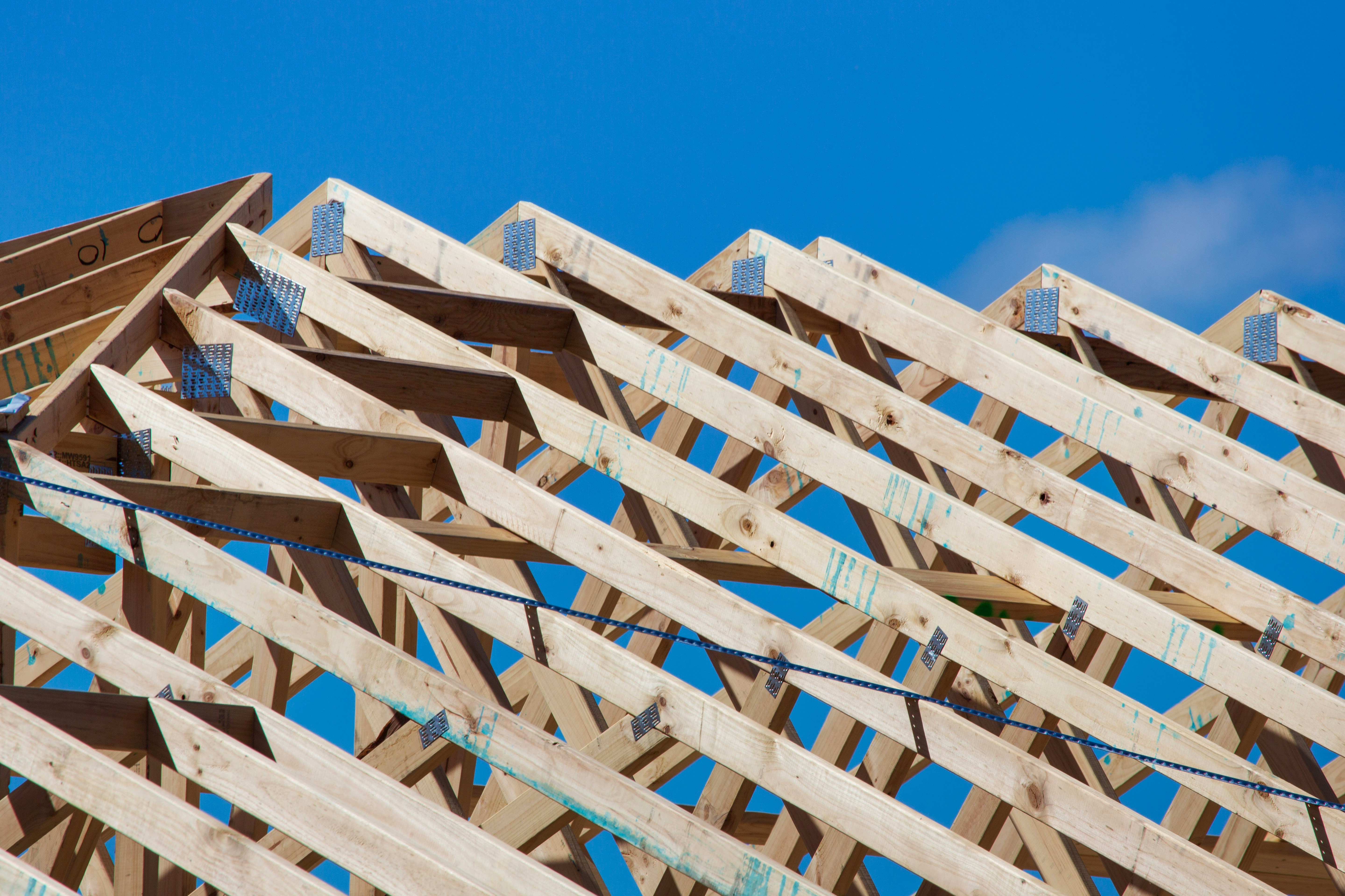 Wooden roof framing structure with metal connectors under a clear blue sky.