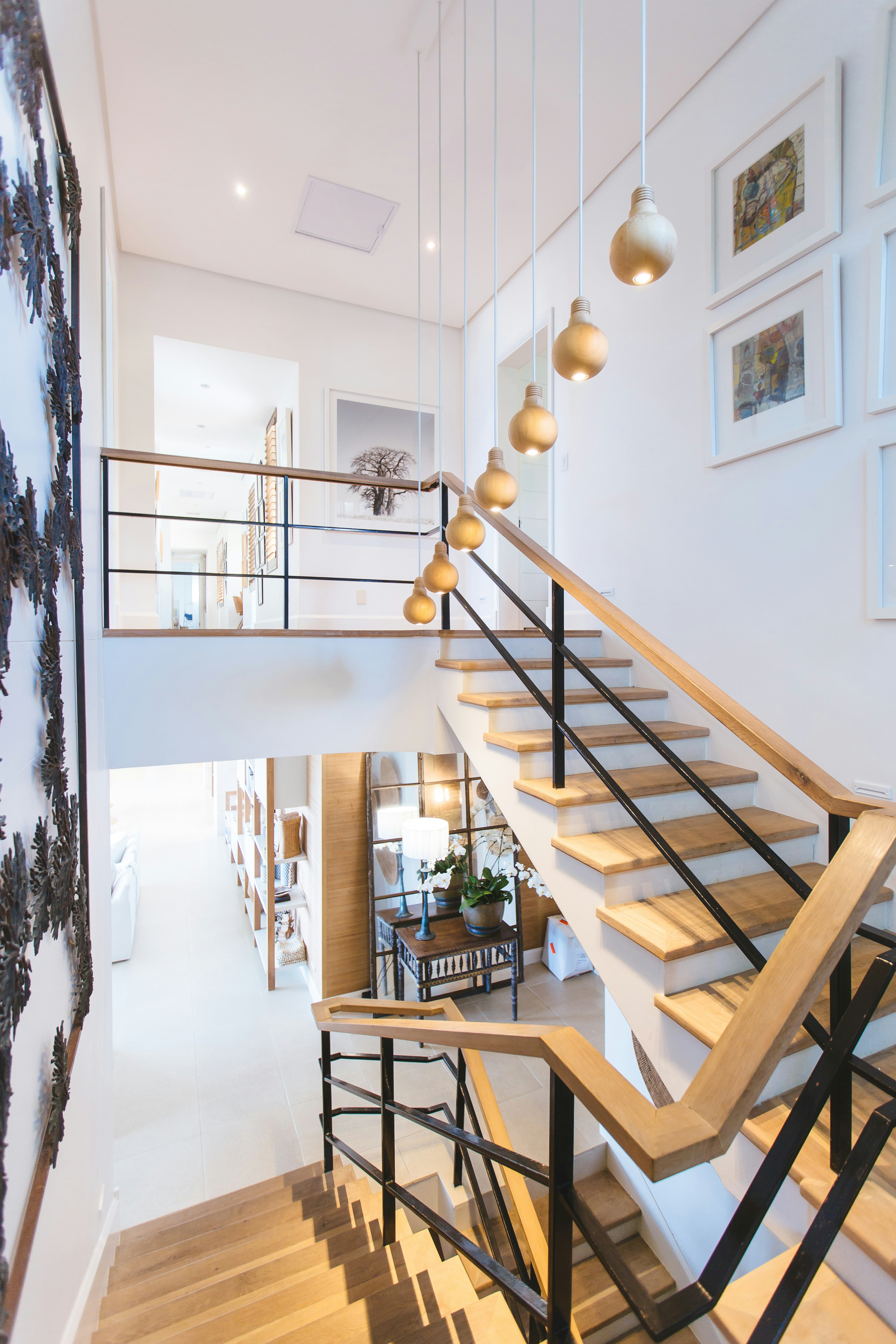 Modern wooden staircase with black metal railing and hanging spherical pendant lights in a bright, white interior.