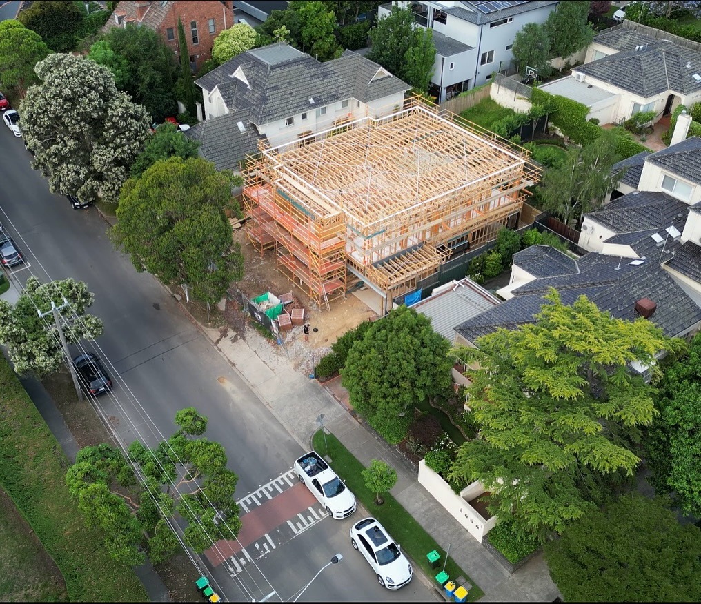 Empty modern kitchen with light wood cabinets, built-in oven, stove, stainless steel sink, and large window overlooking trees.