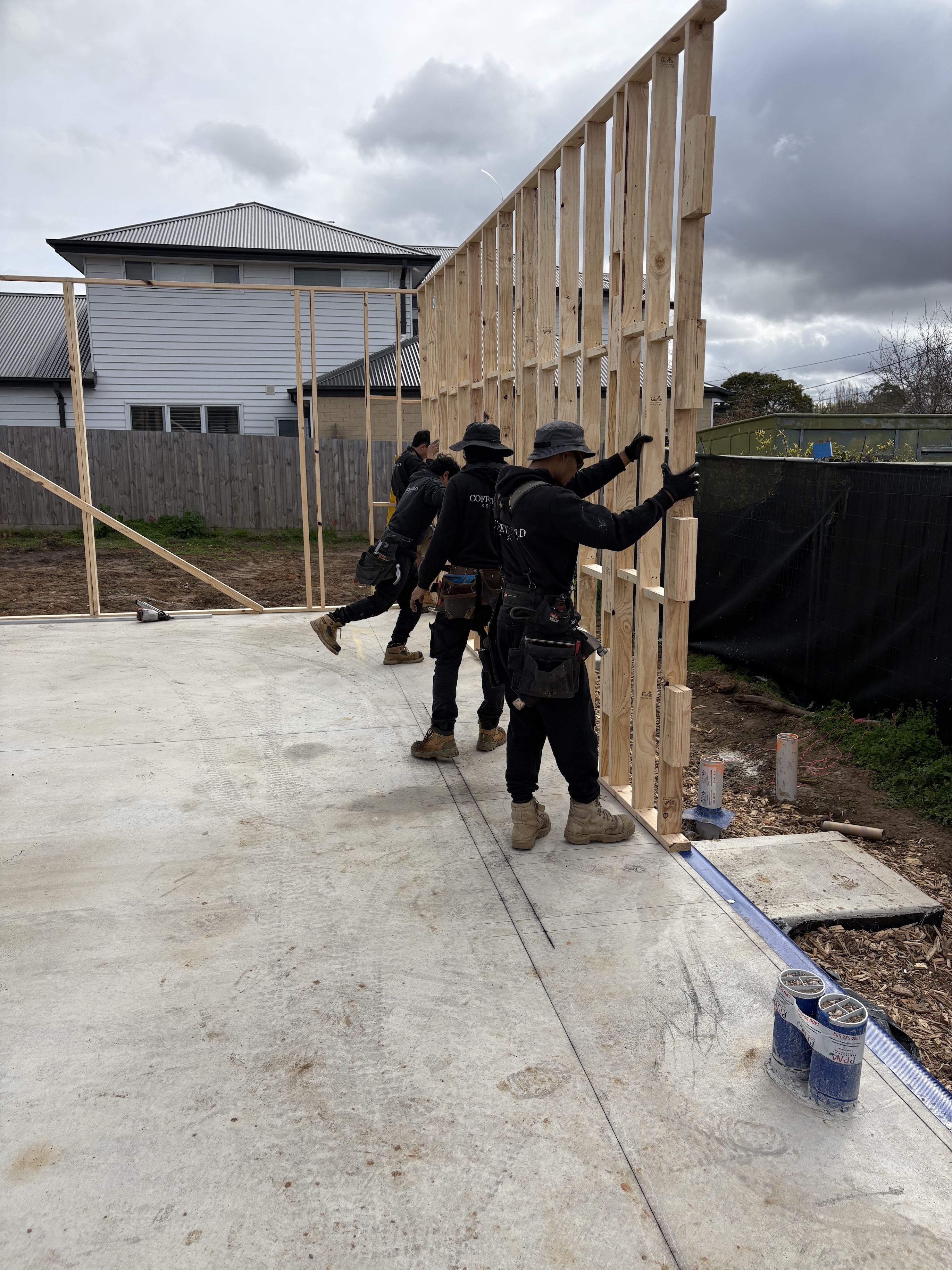 Construction workers installing a wooden frame wall on a concrete foundation at a residential building site.