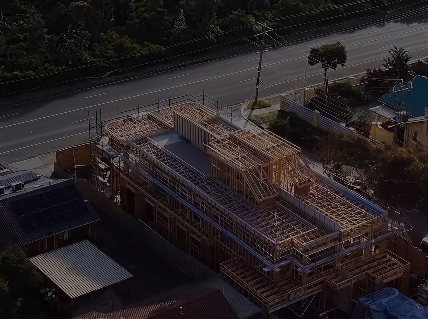 Aerial view of a large wooden building frame under construction next to a road with a car passing by.