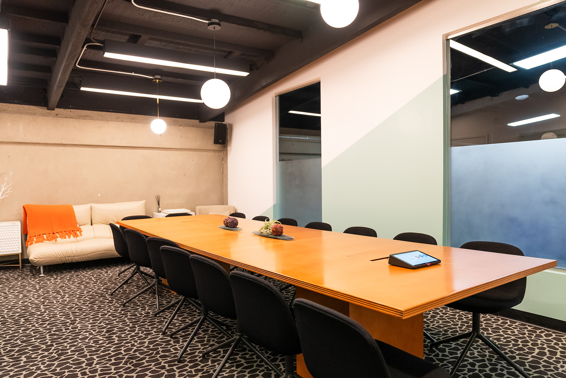 Modern conference room at FutureHouse in San Francisco featuring a long wood table, black chairs, beige sofa with orange throw, and custom giraffe-pattern carpet, designed and built by FrozenFeathers.