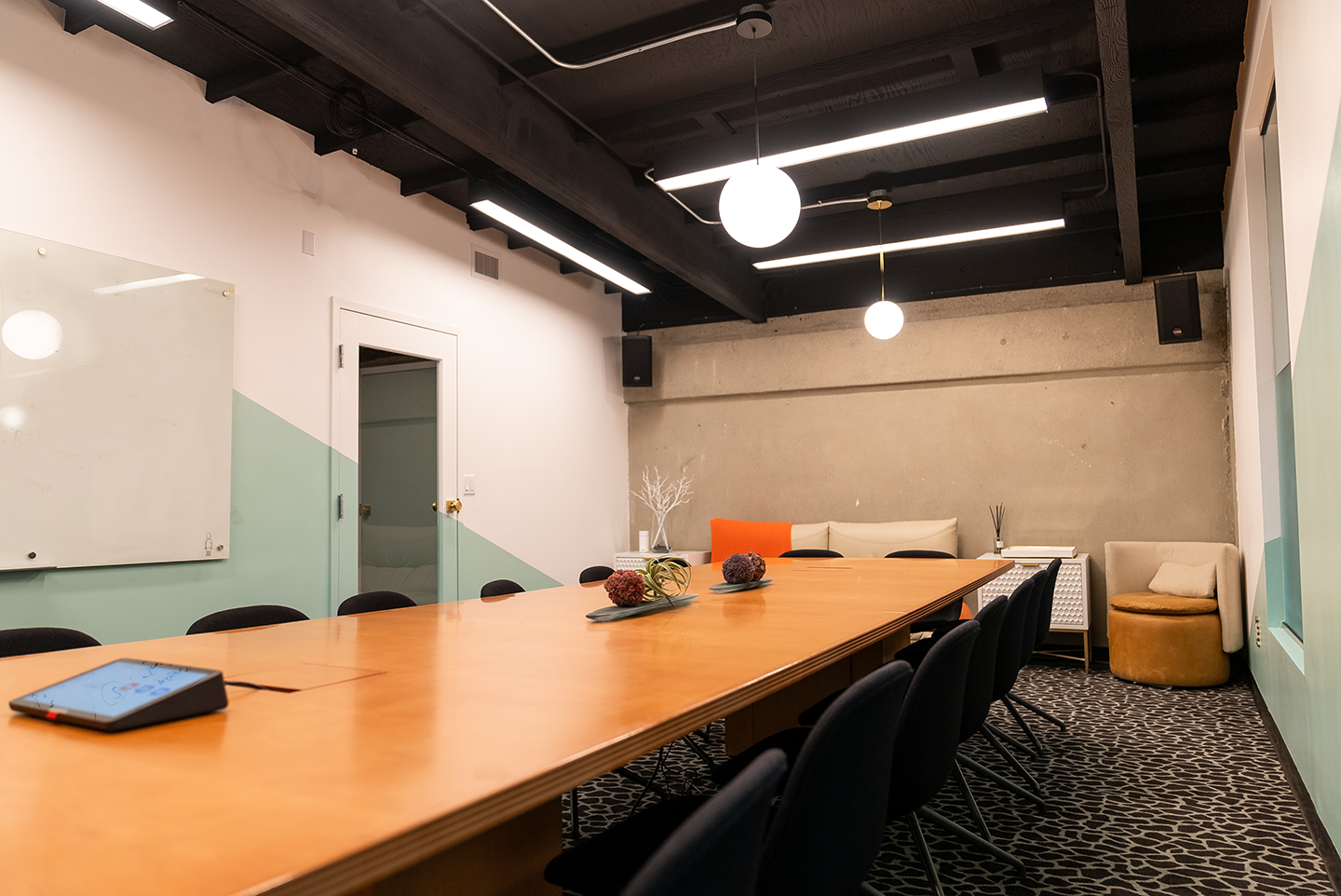 Commercial conference room featuring interior design by FrozenFeathers Studio-a large wooden table, modern black chairs, geometric carpet, and a wall-mounted whiteboard.