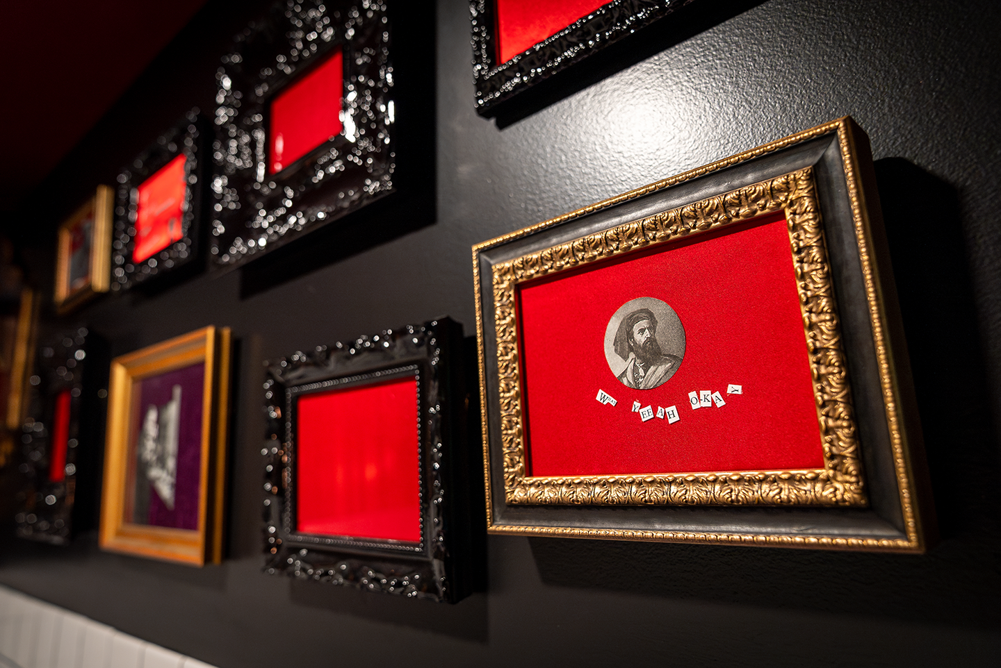 Wall with decorative picture frames, one featuring a vintage portrait on red background and scattered letters.