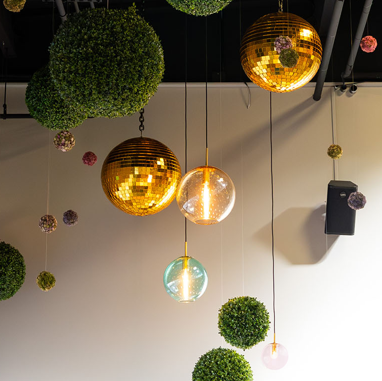 Ceiling decorated with hanging green foliage spheres, golden disco balls, and spherical pendant lights.