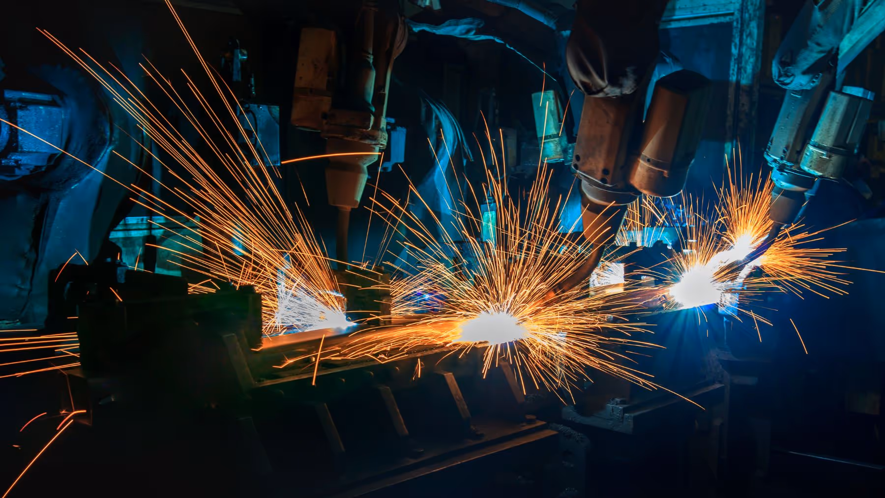 Industrial robotic arms welding metal with bright sparks flying in a dark factory setting.