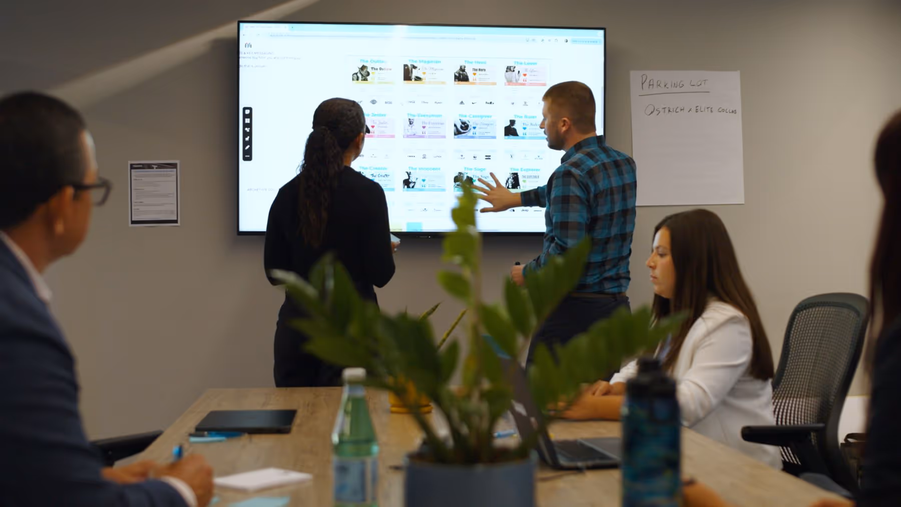 Colleagues in a meeting room presenting and discussing data on a large screen during a work session.