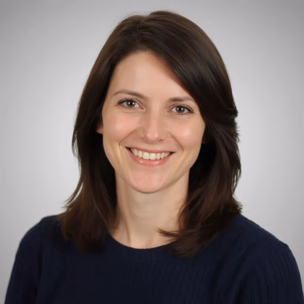 Smiling woman with shoulder-length brown hair wearing a dark blue sweater against a light gray background.