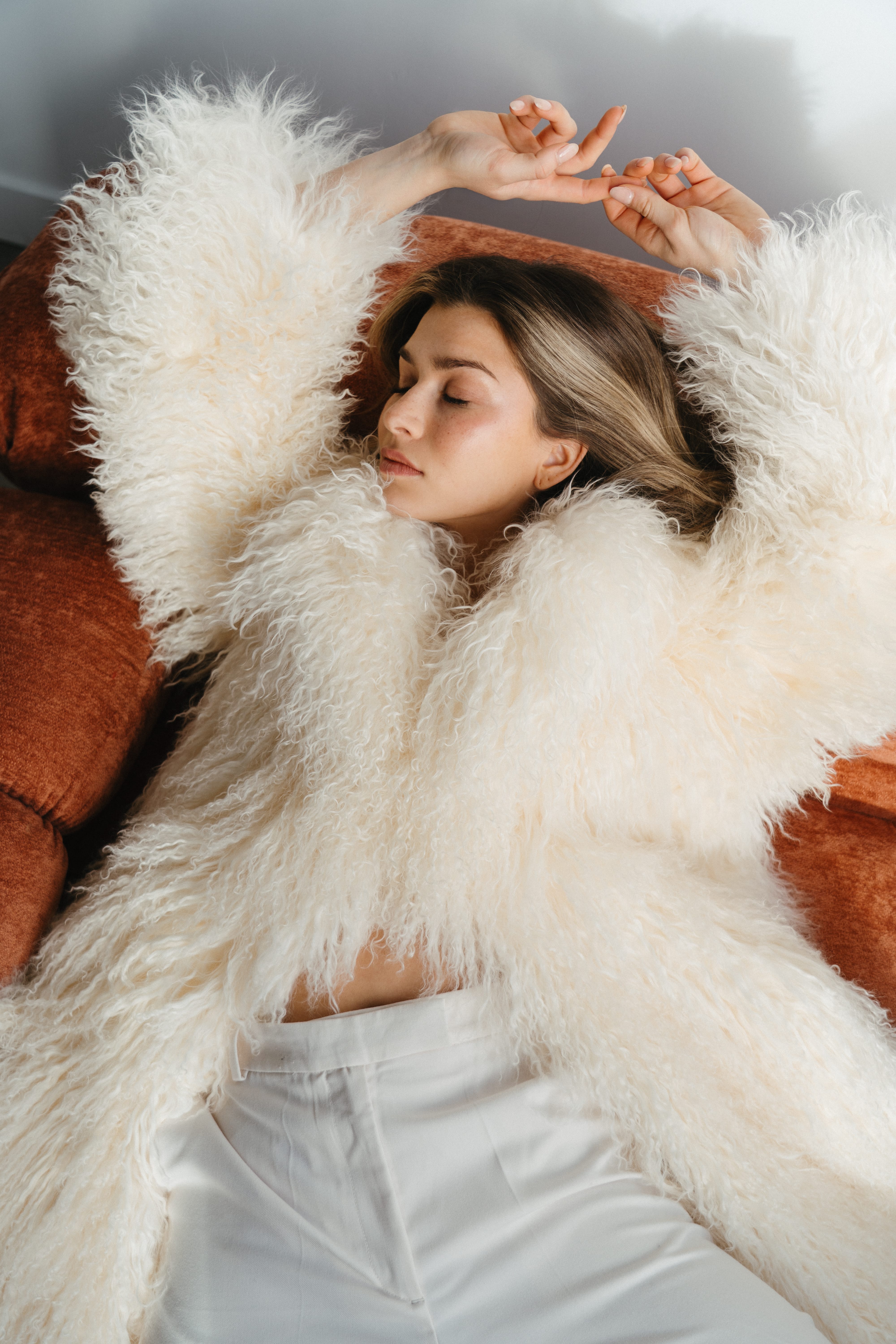 White curvy coffee table with a black Chanel book and a small black vase on top, next to an orange couch on a textured beige carpet.