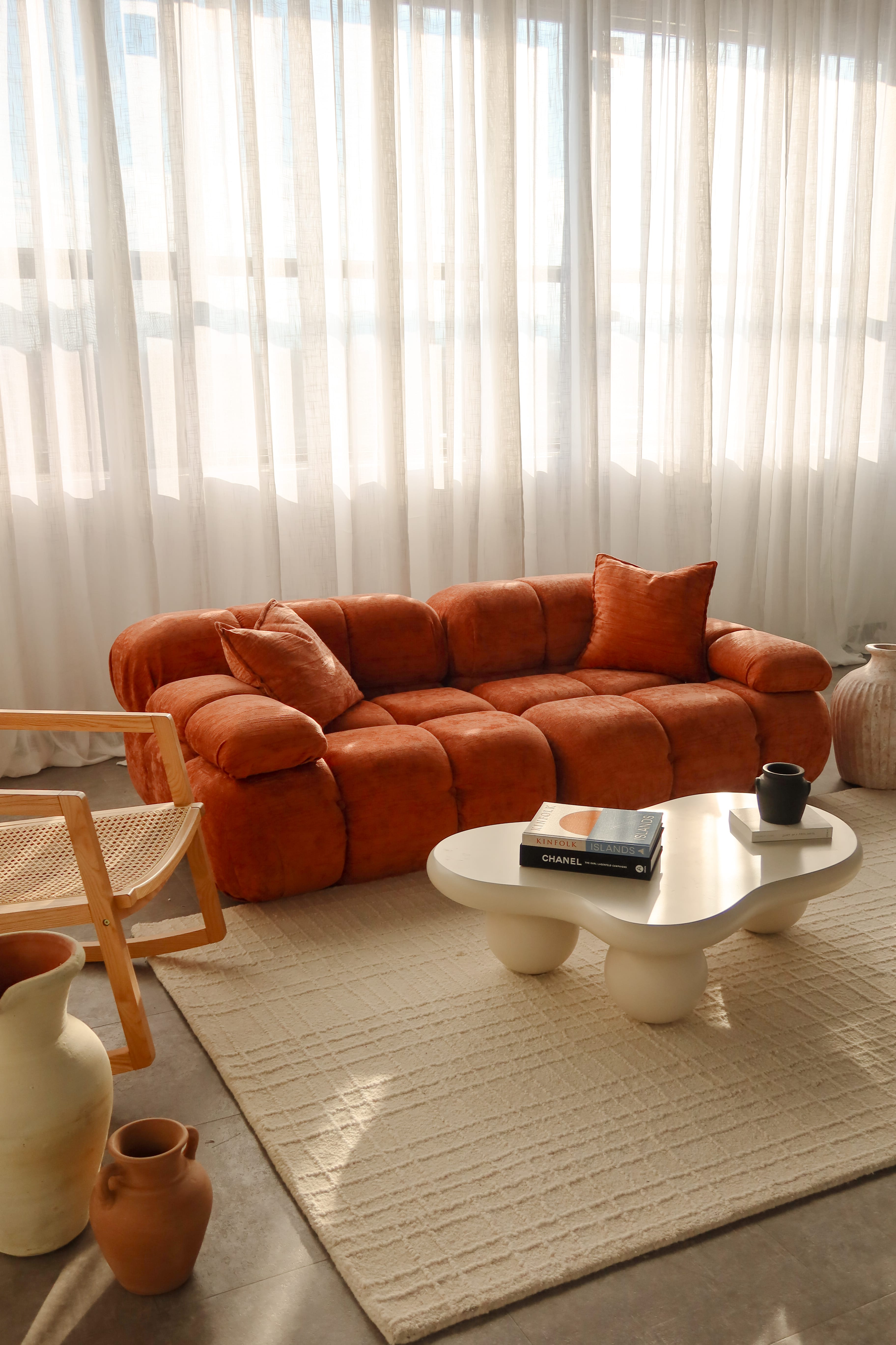 Minimalist photography studio with a black stool on a white backdrop and a modern beige chair beside a window with sheer curtains.