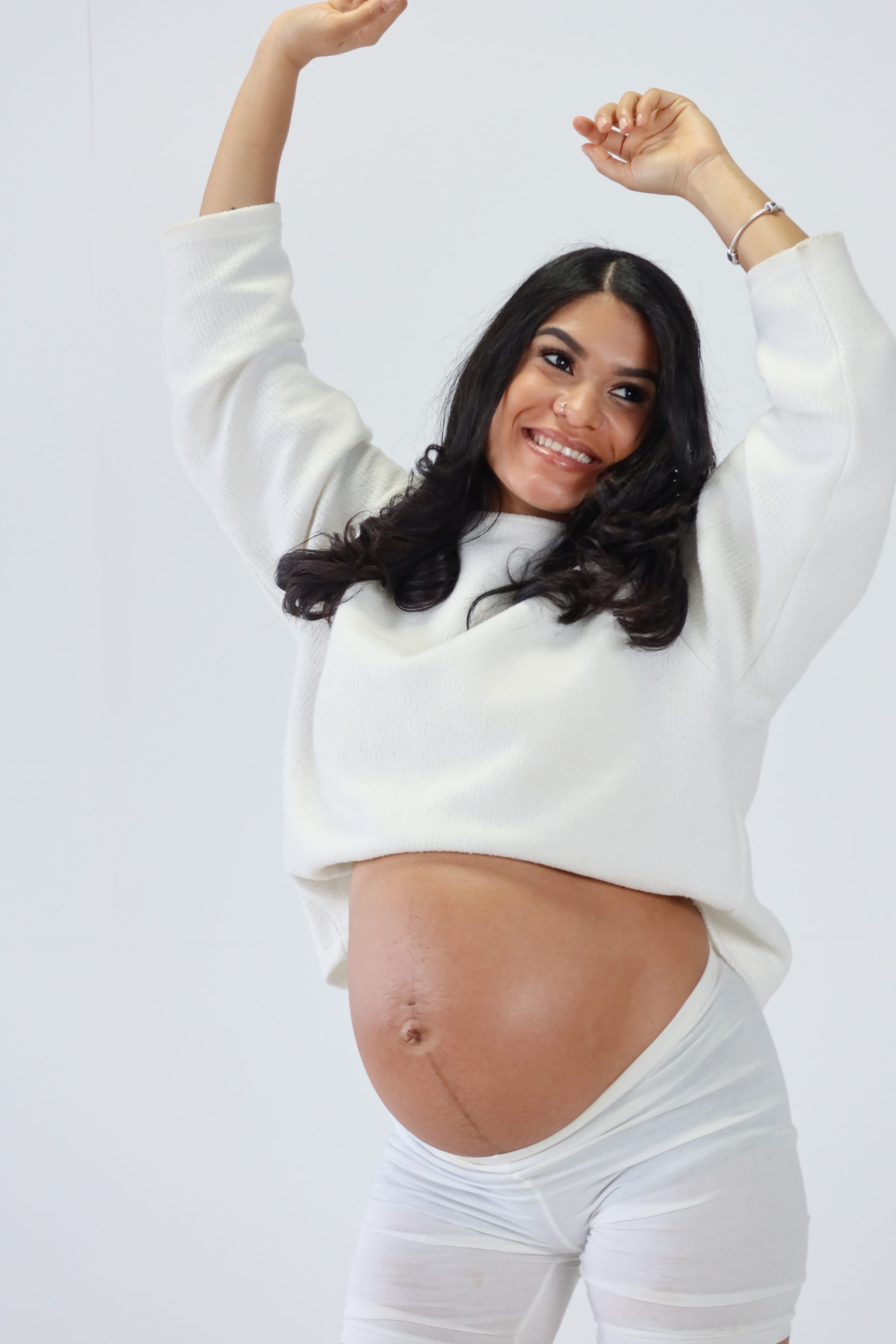 Minimalist photography studio with a black stool on a white backdrop and a modern beige chair beside a window with sheer curtains.
