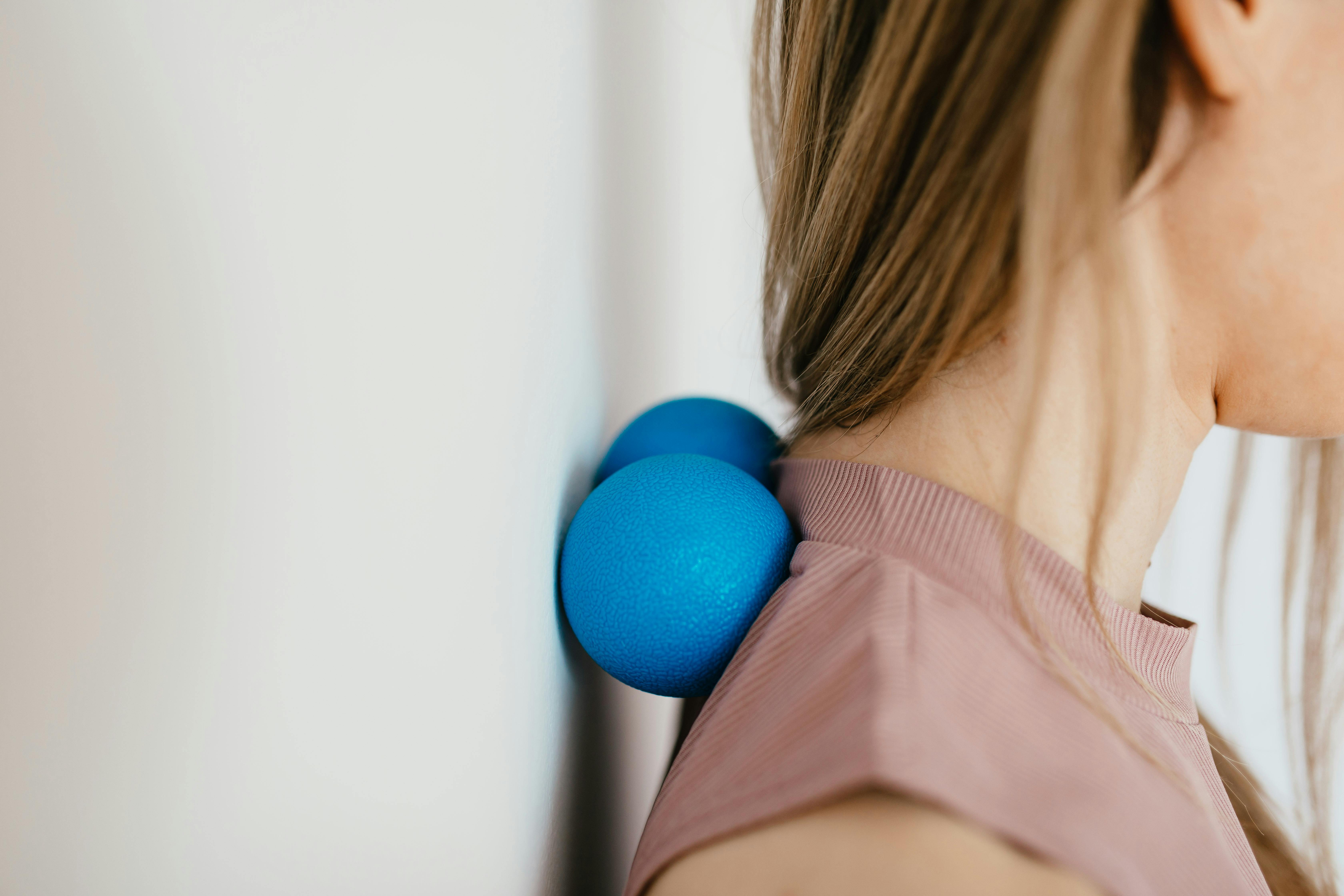 Person pressing a blue massage ballsbetween their neck and a wall for muscle relief.