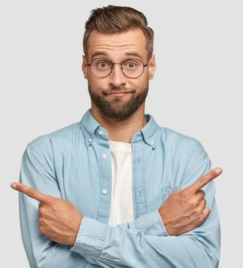 Man with glasses and beard wearing a light blue shirt crossing arms and pointing both index fingers in opposite directions with a puzzled expression.