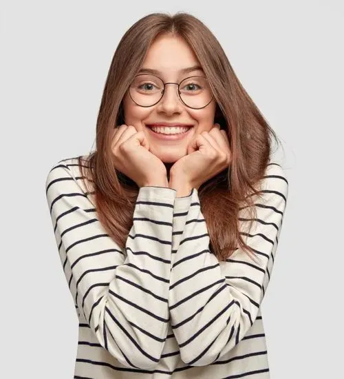 Smiling young woman with long brown hair and glasses wearing a white and black striped shirt, resting her chin on her fists.
