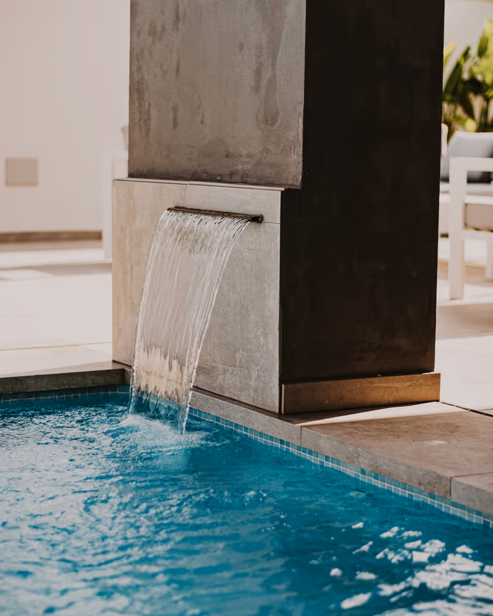 Water flowing from a modern spout into a blue tiled pool on a sunny day.