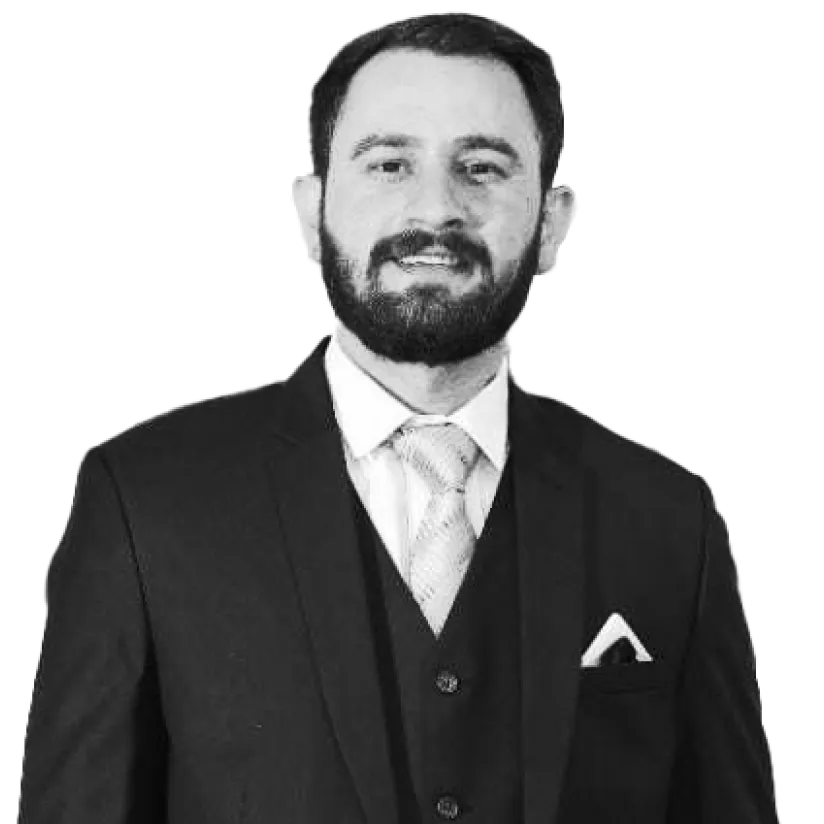 Man with beard wearing a dark suit, light shirt, patterned tie, and a pocket square, smiling at the camera.