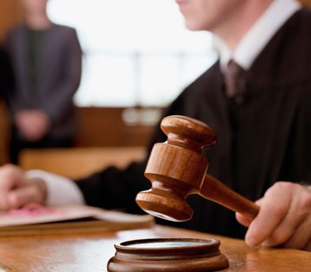 Judge in a courtroom holding a wooden gavel above a sound block.