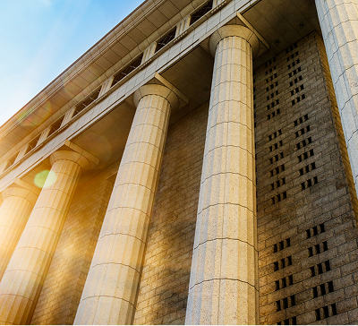 Sunlit exterior view of a classical building with tall stone columns and textured walls.