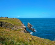 Rocky coastal cliff with green grass overlooking a calm blue ocean under a clear sky.