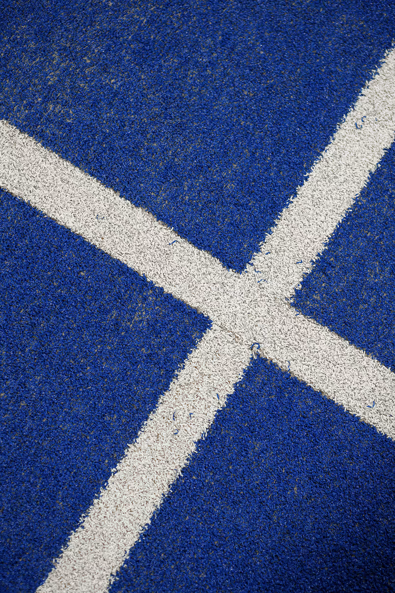 Close-up of textured blue sports court surface with intersecting white boundary lines forming a cross.