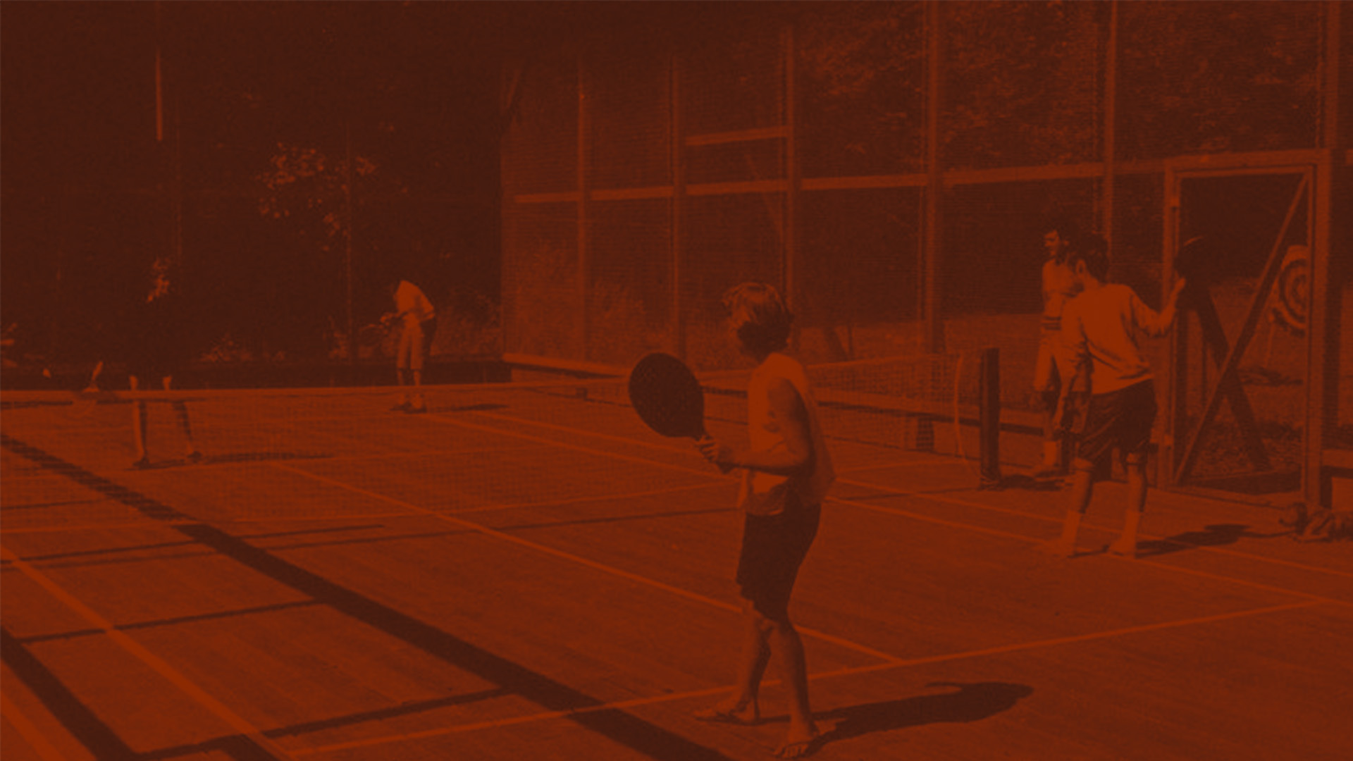 Children playing padel on an outdoor court with paddles and a ball.