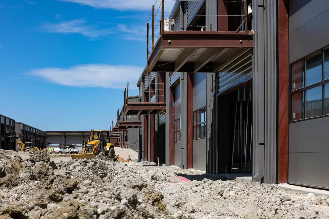 A hand holding a small vial over a robotic apparatus inside a laboratory setup, with visible mechanical components in the background.
