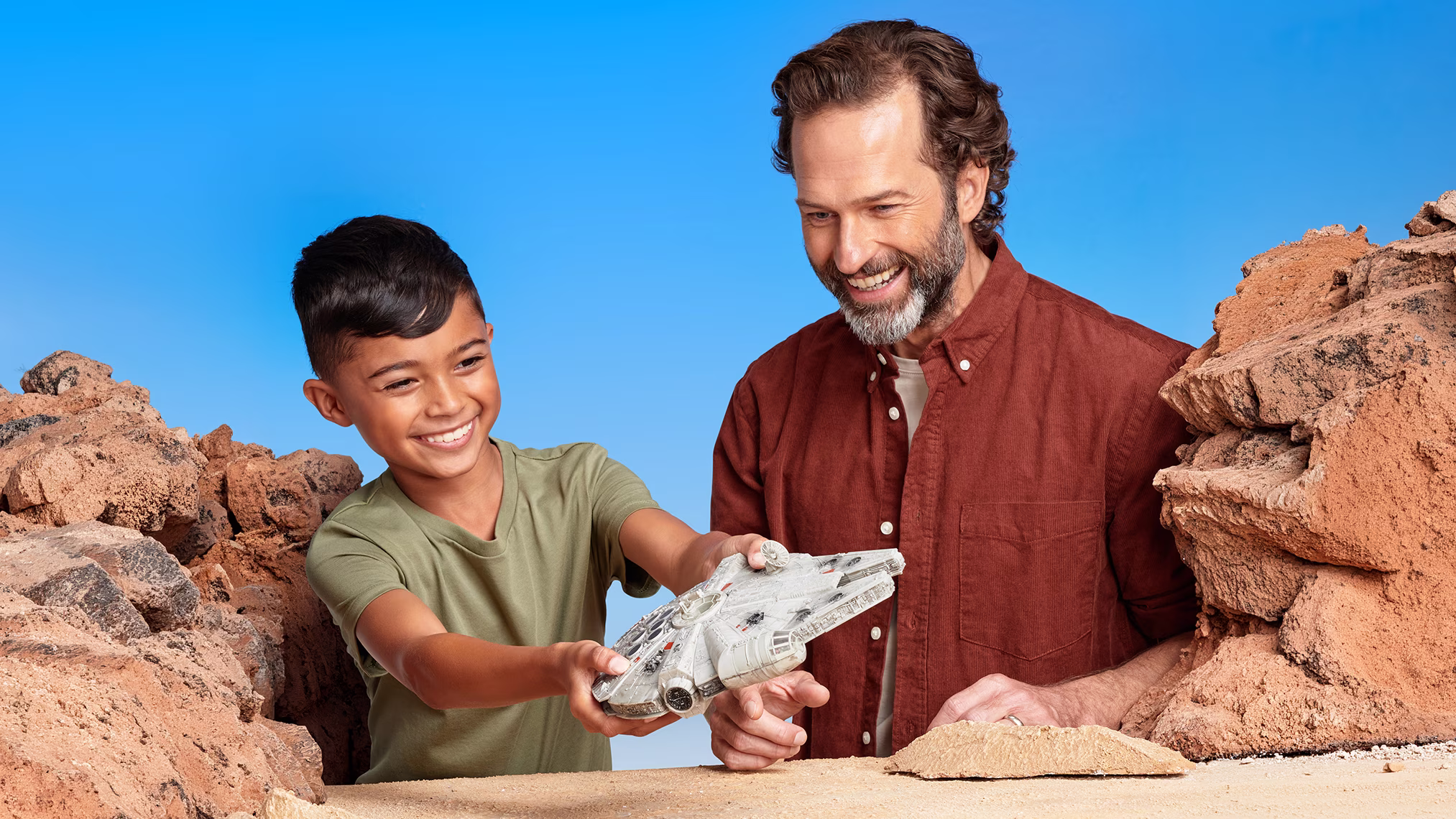 Child and father playing with a Star Wars Millennium Falcon toy in a rocky landscape set